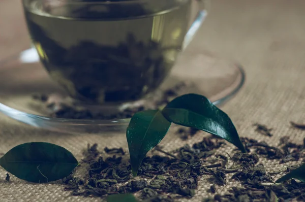 Té seco con hojas verdes en taza, sobre fondo de arpillera —  Fotos de Stock