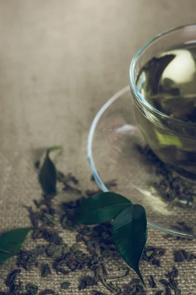 Dry tea with green leaves in cup, on burlap background — Stock Photo, Image