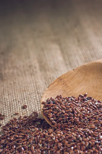 Flax seeds with a wooden spoon on burlap background — Stock Photo, Image