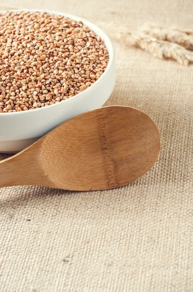 Buckwheat and wooden spoon on burlap background — Stock Photo, Image