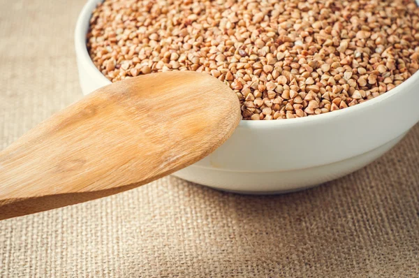 Buckwheat and wooden spoon on burlap background — Stock Photo, Image