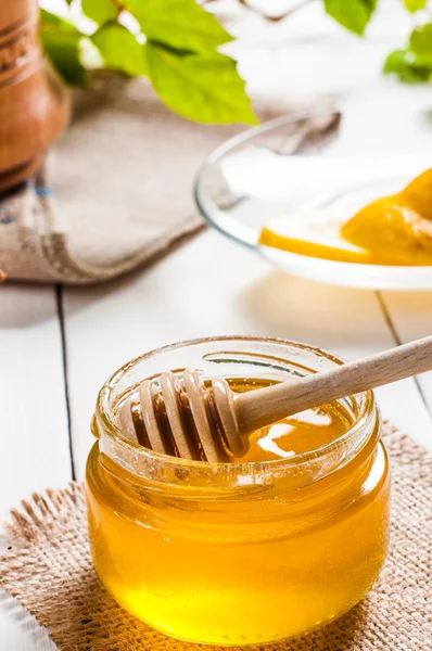 Frasco de mel com dipper e limão fluindo, fundo de madeira — Fotografia de Stock