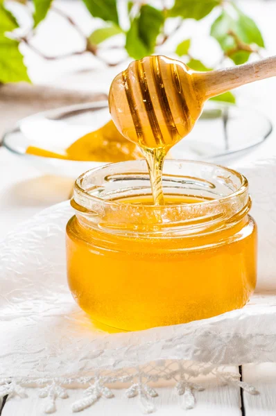 Tarro de miel con cazo y limón fluyendo, fondo de madera — Foto de Stock