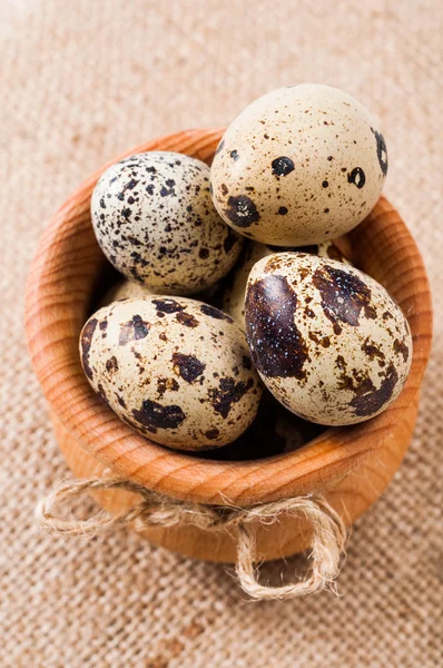 Raw quail eggs in a wooden bowl on burlap background — Stock Photo, Image