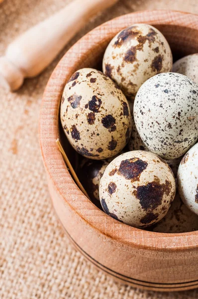 Raw quail eggs in a wooden bowl on burlap background — Stock Photo, Image