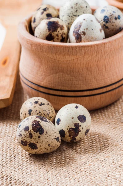 Raw quail eggs in a wooden bowl on burlap background — Stock Photo, Image