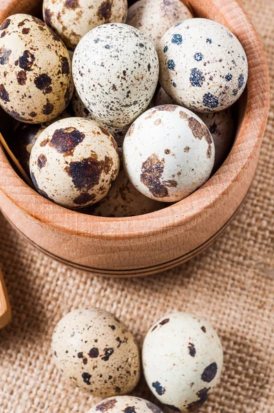 Raw quail eggs in a wooden bowl on burlap background — Stock Photo, Image