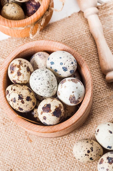 Raw quail eggs in a wooden bowl on burlap background — Stock Photo, Image