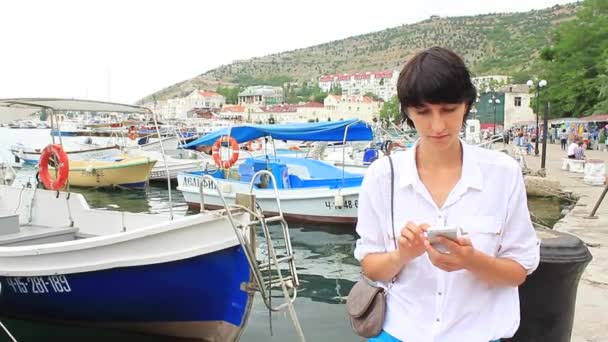 Молодая женщина, использующая мобильный телефон в бухте с моторными лодками — стоковое видео
