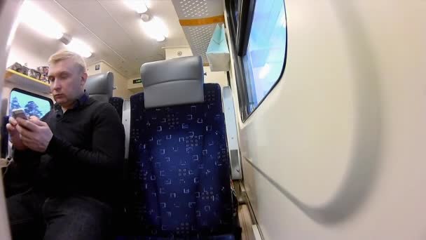 El hombre utiliza un teléfono inteligente en un compartimento de un tren de pasajeros — Vídeos de Stock