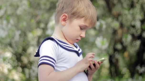 Young little boy plays games on smartphone. Spring park — Stock Video