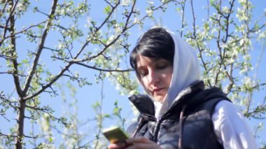 Genç kadın ile smartphone parkta. Bahar. Bir çiçekli ağaç arka planı
