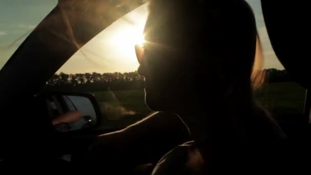 Viento soplando a través de las niñas silueta y el pelo en un coche. Puesta de sol — Vídeos de Stock