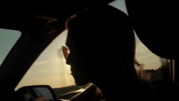 Vent soufflant à travers les filles silhouette et cheveux dans une voiture. Coucher de soleil — Video