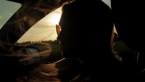 Άνεμος φυσά μέσω κορίτσια σιλουέτα και μαλλιά σε ένα αυτοκίνητο. Ηλιοβασίλεμα — Αρχείο Βίντεο