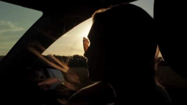 Viento soplando a través de las niñas silueta y el pelo en un coche. Puesta de sol — Vídeos de Stock