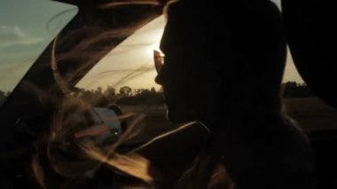 Rüzgar üfleme ile kızlar siluet ve saç bir arabanın içinde. Günbatımı