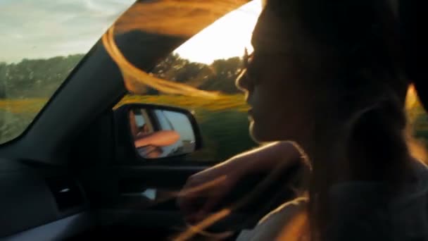 Der Wind weht im Auto durch die Silhouette und die Haare der Mädchen. Sonnenuntergang — Stockvideo