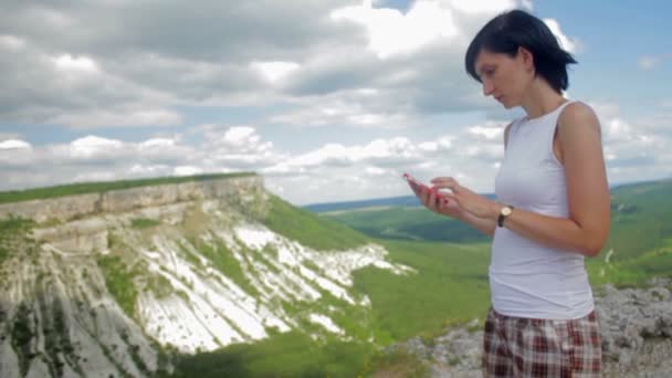 Mulher atraente mensagens de texto no smartphone em um fundo de montanhas — Vídeo de Stock
