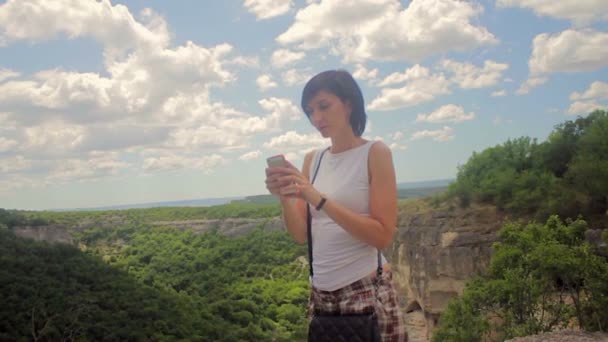 Привлекательная женщина делает селфи на смартфоне на фоне гор — стоковое видео