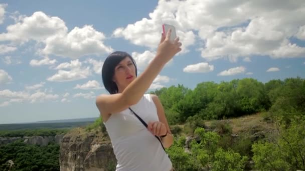 Привлекательная женщина делает селфи на смартфоне на фоне гор — стоковое видео