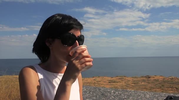 Kobieta, biorąc łyk kawy przez morze w tle latarni morskiej — Wideo stockowe