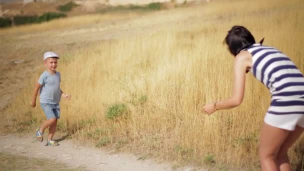 Un ragazzo carino corre lungo il campo alle sue madri a braccia aperte mentre la telecamera lo segue . — Video Stock