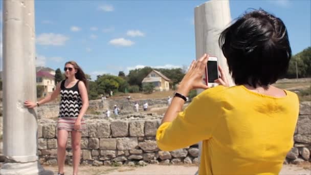 Happy women taking photo girl friend with smartphone on the ruins of the ancient city background — Stock Video