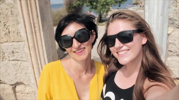 Dos amigas jóvenes tomando selfie en el mar y las ruinas del fondo de la antigua ciudad — Vídeo de stock