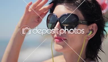 Deniz arka planda müzik güneş gözlüğü ve kulaklık ile güzel genç kadın portresi kapatın