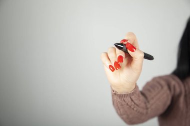 Siyah bir kalem tutan genç bir kadın ve açık bir arkaplan üzerine bir şeyler yazıyor.