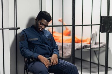 Güçlü bir siyah gardiyan hapishane koridorundaki mahkumlarla birlikte hücreleri koruyor.