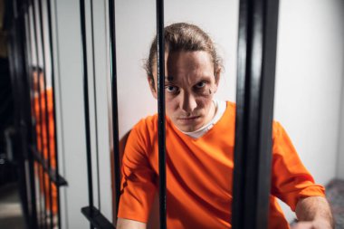 Dövmeli vahşi suçlu manyak demir parmaklıkları tutuyor. Bir hapishane hücresinde yakın plan bir portre..