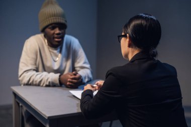 A black guy listens to his rights from a civil lawyer at a table in a visiting room in a state prison clipart