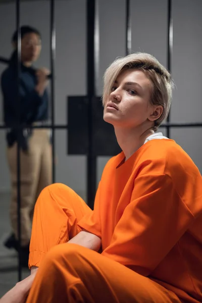 A beautiful young girl is placed under arrest in an asian prison. Sitting in a cell. In the background a female warden. — Stock Photo, Image