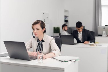 Müdür, büyük bir şirketin açık alan ofisindeki bir masada ofis işiyle meşgul..