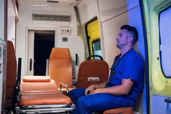 Tired paramedic on duty, sitting in an ambulance car, waiting for the next call