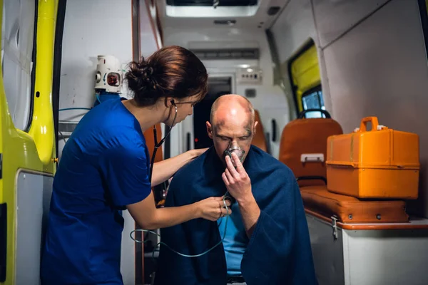 Молодой врач со стетоскопом ухаживает за своим раненым пациентом в машине скорой помощи — стоковое фото
