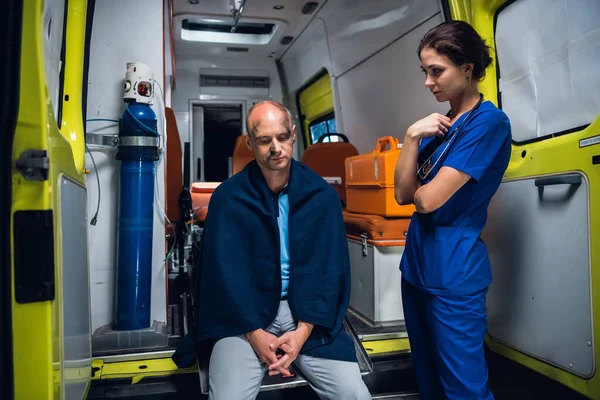 Медсестра, стоящая рядом с пациентом, который сидит на краю машины скорой помощи — стоковое фото