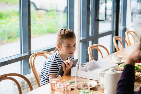 Une jolie fille est assise à une table avec une tablette. Backg flou — Photo