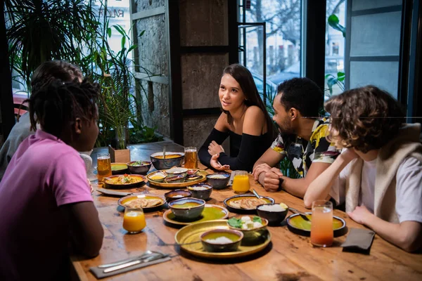 Een groep studenten zit aan de tafel in een café, chatten, ha — Stockfoto