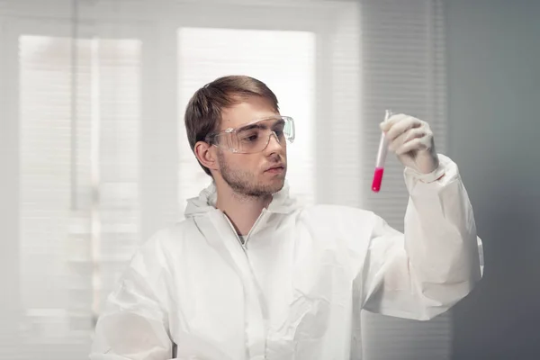 Um retrato de um jovem cientista em óculos de proteção segurando um tubo de ensaio com um líquido vermelho — Fotografia de Stock