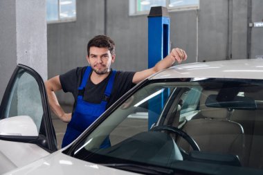 Bir araba servisi çalışanı beyaz bir arabanın yanında duruyor.