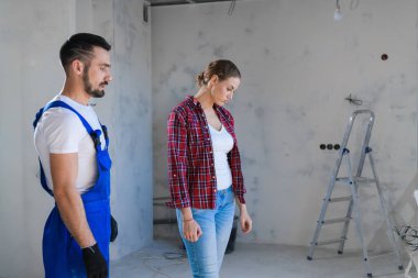 Bayan müşteri, kötü tamirat için mavi tulumlu işçiyi azarlıyor.