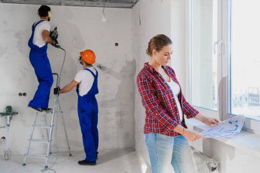 Müşteri dairenin düzenini inceliyor, inşaatçılar merdiveni deliyor.