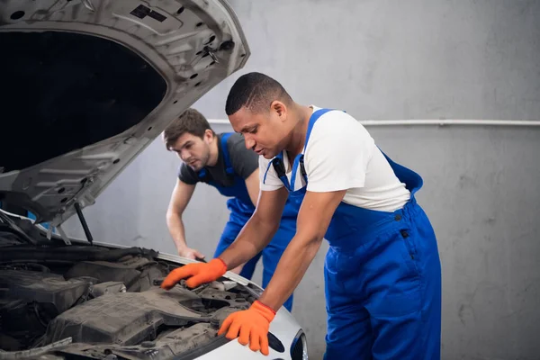 Dos trabajadores masculinos inspeccionando el motor de un coche — Foto de Stock