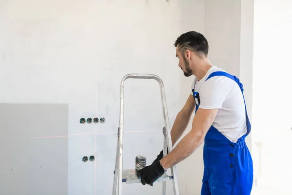 O trabalhador de macacão move a escada para a parede — Fotografia de Stock