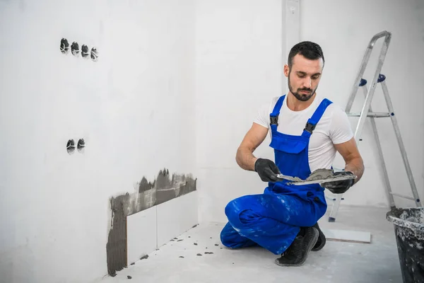 Voorman in blauw uniform zet tegels op de badkamer muur — Stockfoto