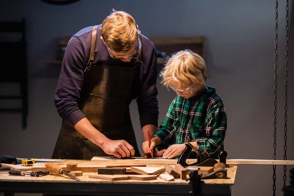 Un padre joven y su hijo pequeño hacen un juguete de madera en un taller de carpinteros. — Foto de Stock