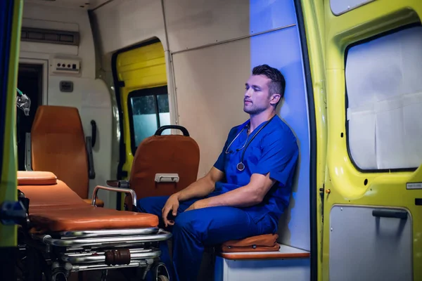 Médico con uniforme médico sentado con los ojos cerrados dentro del coche ambulancia —  Fotos de Stock